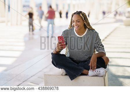 Happy Black Woman Using A Smartphone Outdoors, Wearing Her Hair In Braids.