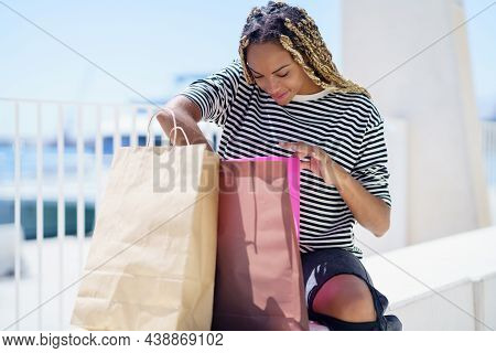 Black Female Looking For Something In Her Shopping Bags In A Shopping Street, Hairstyle With Braids.