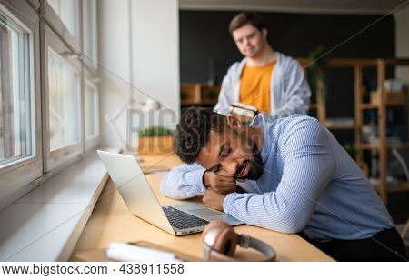 Tired Young African-american Teacher Sleeping With Head On Desk Indoors In Staffroom.