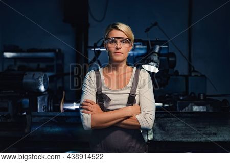 Portrait Of Mid Adult Woman Standing With Arms Crossed Indoors In Metal Workshop, Looking At Camera.