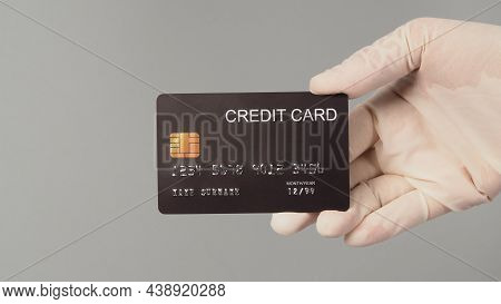 Hand Is Wear White Medical Glove And Holding Black Credit Card Isolated On Grey Background.
