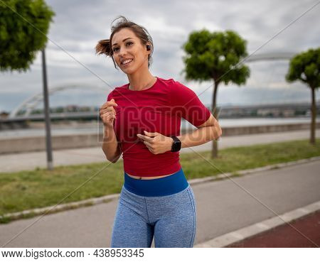 Active Woman Smiling Exerising Outdoors. Young Athlete Listening To Music Running Jogging With Bridg