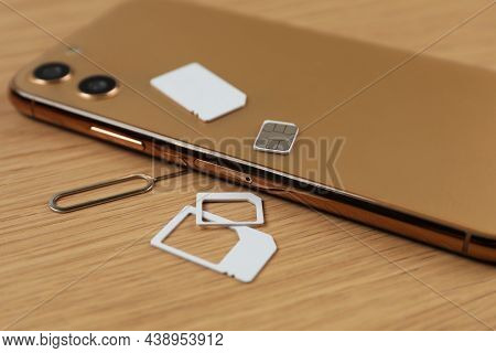 Sim Cards, Mobile Phone And Ejector Tool On Wooden Table