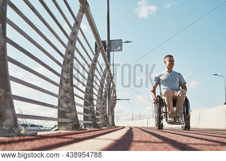 Full Length Portrait Of Adult Man In Wheelchair In Accessible City Environment Outdoors In Sunlight,