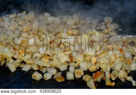 Hash browns being cooked on a griddle, with steam rising from the small cubed potatoes