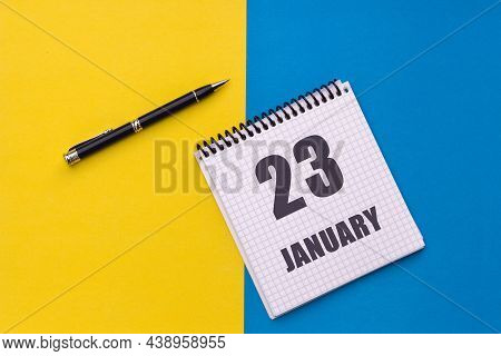 January 23th. Day 23 Of Month. Calendar Date. Notebook With A Spiral And Pen Lies On A Yellow-blue B