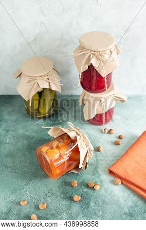 Pickles, Canned Vegetables In A Glass Jars, One Jar On Its Side, Scattered Nuts And A Napkin On A Gr