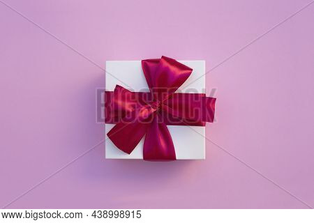 White Gift Box With Red Ribbon On A Lilacbackground. Valentines Day Backdrop. Flat Lay Style With Mi