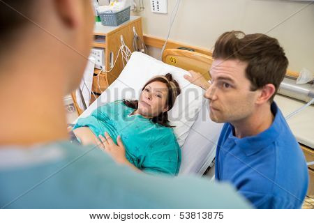 High angle view of mid adult pregnant woman and husband looking at nurse in hospital room