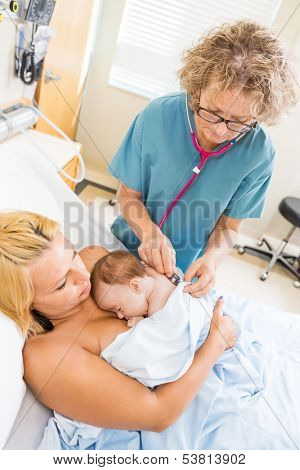 Mature nurse examining newborn babygirl with stethoscope in hospital room