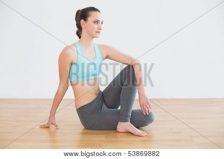 Full length side view of a fit young woman sitting in cowface posture in fitness studio