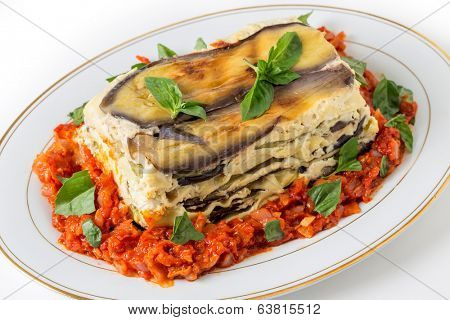 Vegetable lasagne, made with courgettes and eggplants (zucchini and aubergines), pasta sheets and bechamel sauce, served with a tomato and onion sauce and a basil garnish.