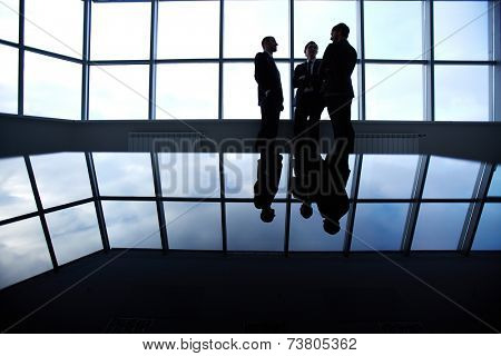 Three business partners having a discussion standing against a panoramic window in office 