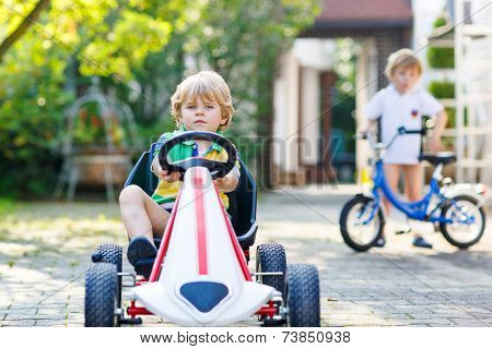 Active Little Boy Driving Pedal Car In Summer Garden