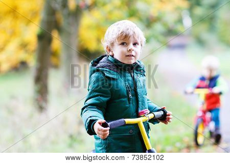 Two Little Sibling Boys Having Fun On Bikes In Autumn Forest.