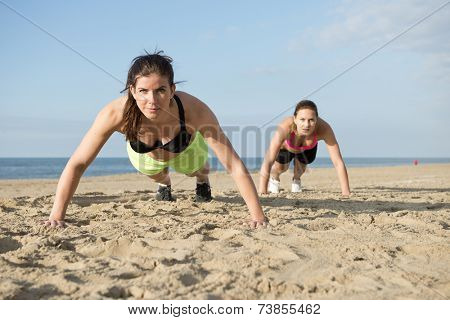 Two women doing pushups on a beach during an intense workout