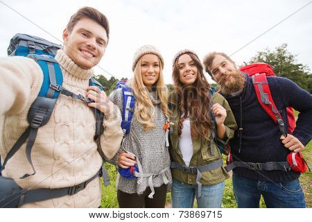 adventure, travel, tourism, hike and people concept - group of smiling friends with backpacks making selfie outdoors