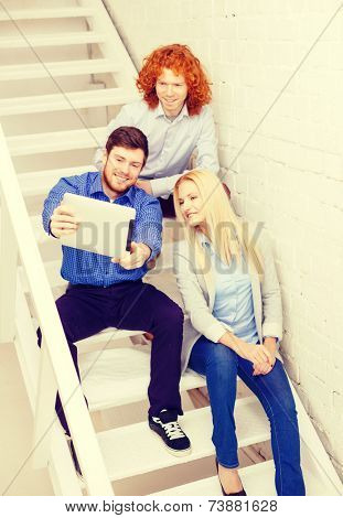 business, technology and startup concept - smiling creative team with tablet pc computer sitting on staircase