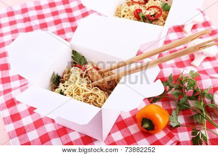 Chinese noodles and sticks in takeaway boxes on fabric background