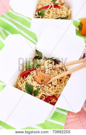 Chinese noodles and sticks in takeaway boxes on green napkin on pink background
