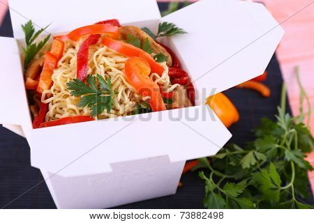 Chinese noodles in takeaway box on black mat on pink background