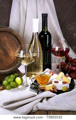 Supper consisting of Camembert and Brie cheese, honey, wine and grapes on napkin and wine barrel on curtain background
