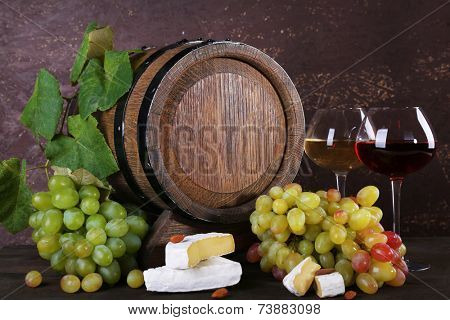 Wine in goblets, Camembert and brie cheese, grapes and wooden barrel on wooden table on wooden background