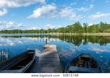 White Clouds On The Blue Sky Over Blue Lake With Boats And Boardwalk