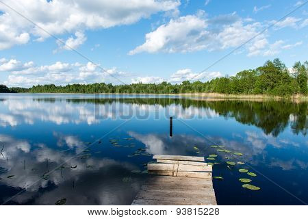 White Clouds On The Blue Sky Over Blue Lake With Boats And Boardwalk