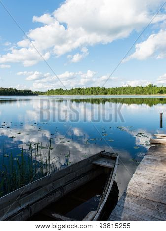 White Clouds On The Blue Sky Over Blue Lake With Boats And Boardwalk