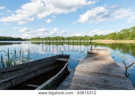 White Clouds On The Blue Sky Over Blue Lake With Boats And Boardwalk