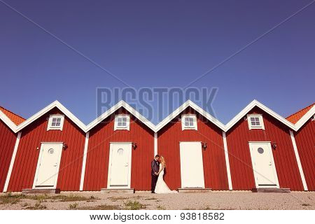 Bride And Groom Near Red Houses In A Rpw