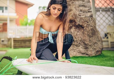 Surfer woman with bikini and wetsuit waxing surfboard