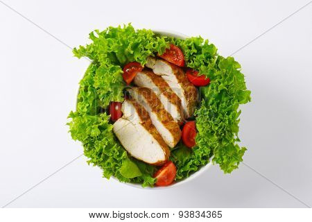 bowl of sliced chicken breasts with lettuce and cherry tomatoes on white background