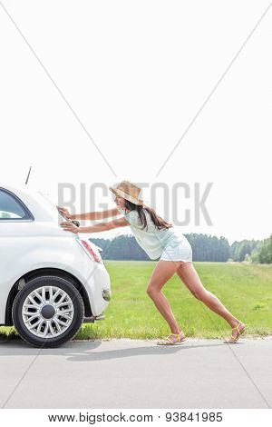 Full-length of woman pushing broken down car on country road