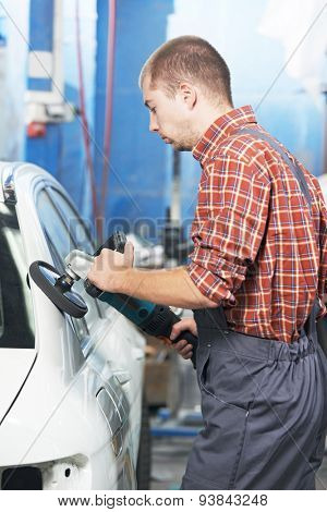 auto mechanic worker polishing car body at automobile repair and renew service station shop by power buffer machine