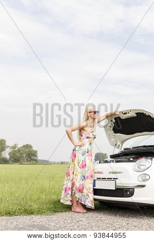 Full-length of tensed woman standing by broken down car on country road