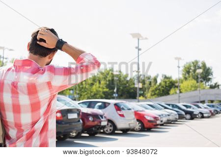 Rear view of man with hand behind head standing on city street against clear sky