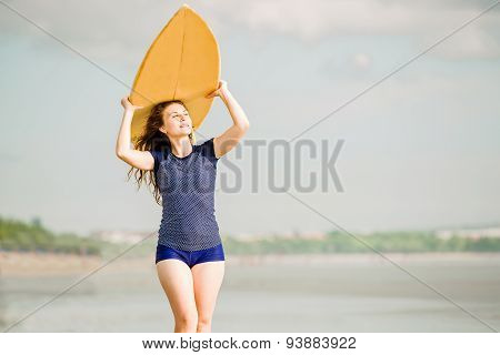 Beautiful sexy surfer girl on the beach at sunset walks along ocean shore, yellow surfboard in her h