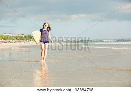 Beautiful sexy surfer girl on the beach at sunset walks along ocean shore, yellow surfboard in her h