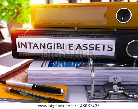 Black Ring Binder with Inscription Intangible Assets on Background of Working Table with Office Supplies and Laptop. Intangible Assets Business Concept on Blurred Background. 3D Render.
