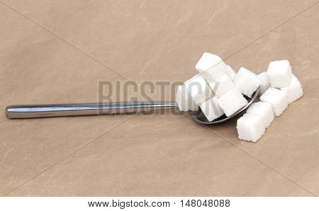 Big pile of white sugar cubes on silver spoon overflowing on the side