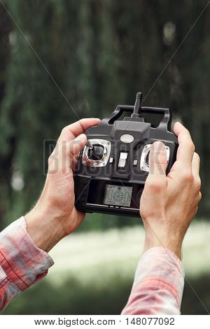 Remote control for unmanned drone, close-up. Transmitter for controlling moving device in male hands, blurred nature background. Electronics, hobby, aeromodelling concept