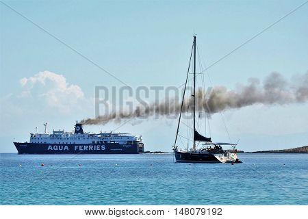 Alonissos, Greece - June 28, 2016: Cruise Aqua ferry ship on sea with big black smoke streak line from its chimneys, in contrast to a small fishing boat.