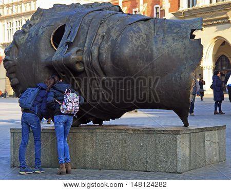 Krakow, Poland - October 29, 2015: tourists are exploring head sculpture Eros Bendato by polish artist Igor Mitoraj on Market Square in Krakow, Poland