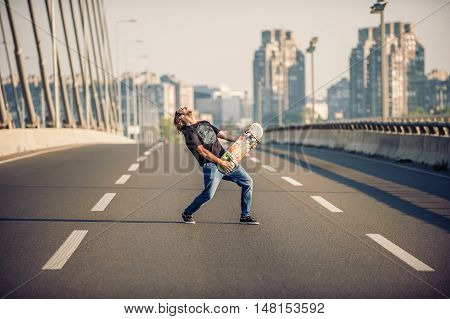 Happy Skateboarder On The Bridge Playing Guitar On His Skate Board
