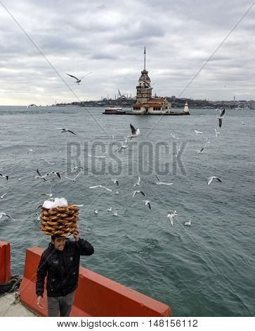 Istanbul Turkey - December 04 2013: Maiden Tower. A young salesman (Simit) bread vendor. European part of Istanbul in the background against the shore. Left Blue Mosque medium Hagia Sophia Topkapi palace dome seem right. The Maiden's Tower (Turkish: Kiz K
