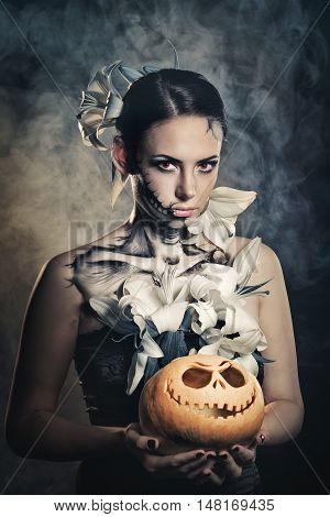 Young attractive girl with creative make-up for Halloween. Portrait close-up pumpkins. Mysterious and frightening image of lilies and red eyes. Witchcraft. Dreadful. Jack-o'-lantern