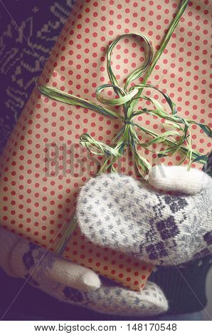 Girl holds in hands Christmas present. Christmas background. Gifts for men. Knitted mittens. Knitted dress. Box with gifts. Merry Christmas. Toned image.
