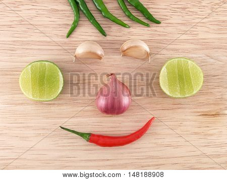 smiley face shape (hair, eyes, ears, nose and mouth) of colorful organic spice vegetables on wooden kitchen table, prepare ingredient for thai food, cooking happily concept, flat lay close up top view